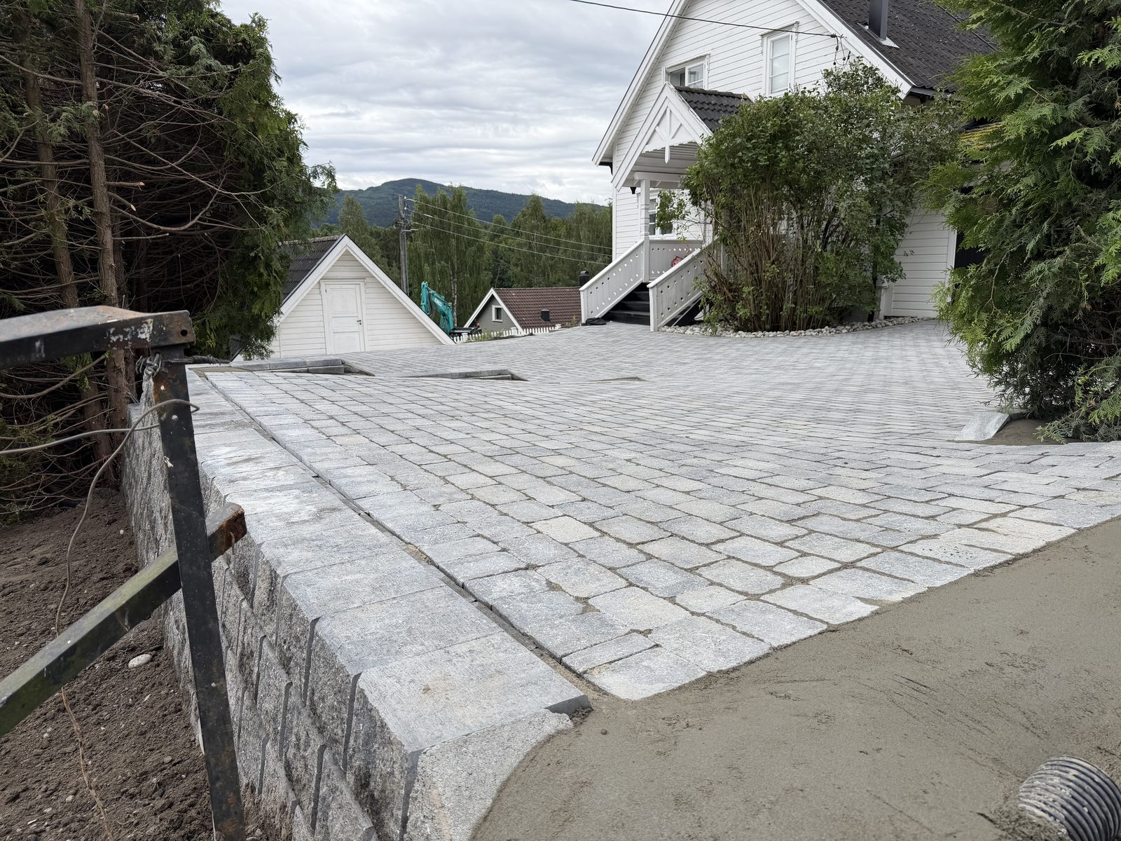 Ny forstøtningsmur i granittblokk med belegningsstein foran hvitt hus